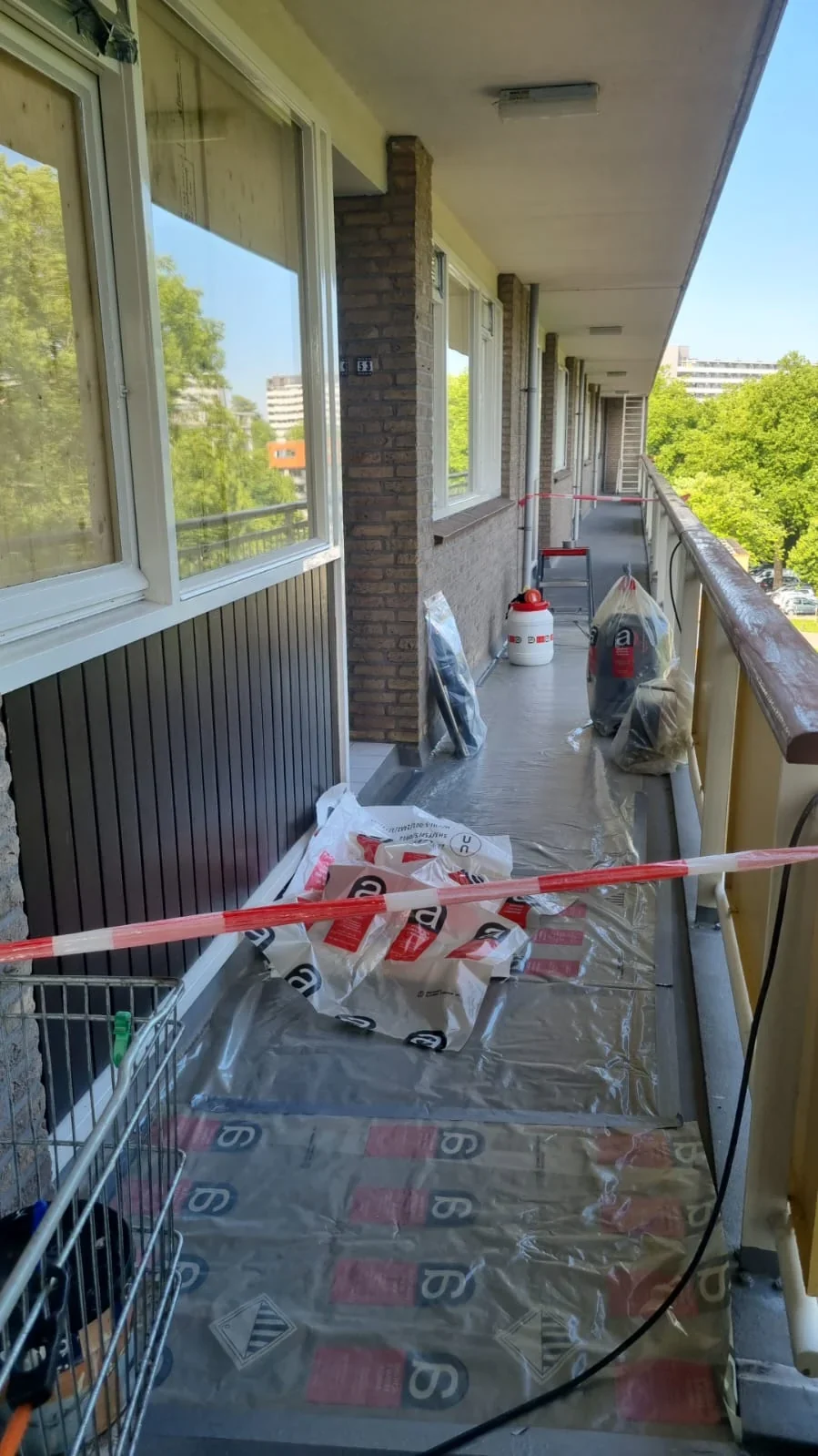 Afgezette galerij met afgedekte vloer en verpakte materialen tijdens het project aan de Toon Verheystraat in Schiedam