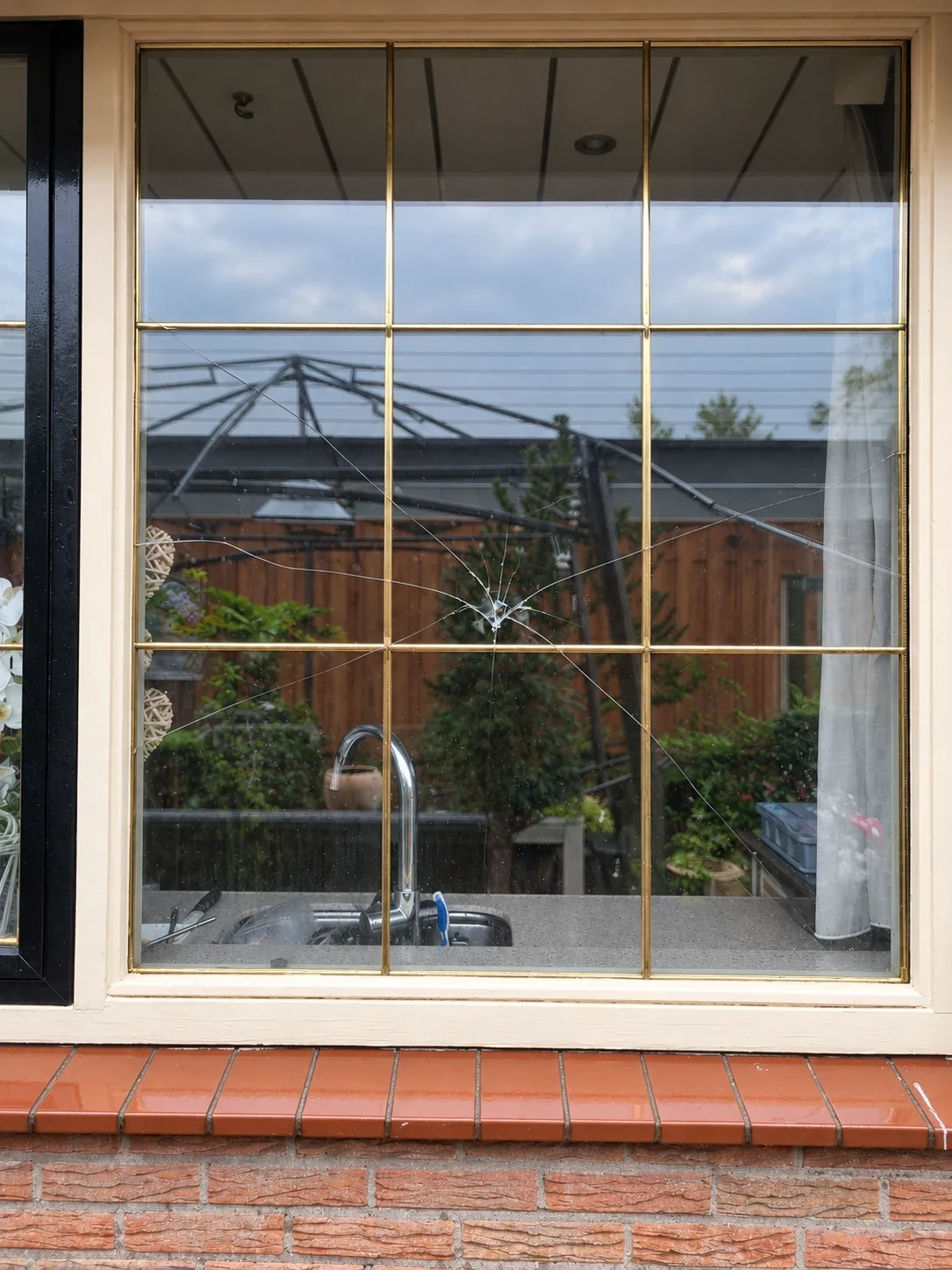 Gebarsten isolatieruit in een wit houten kozijn in Rozenburg, met duidelijk zichtbare barsten en een raamverdeling van messing roeden